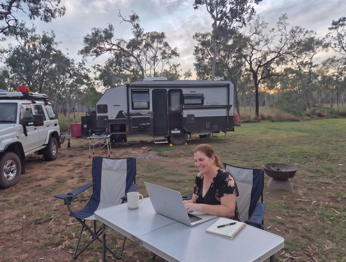 Anna, founder of Allsorted Digital, working on her laptop at a fold-out table beside her caravan and 4WD at a bush campsite in regional WA